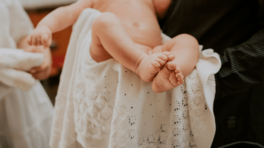 A baby wrapped in a white blanket being held by an adult.