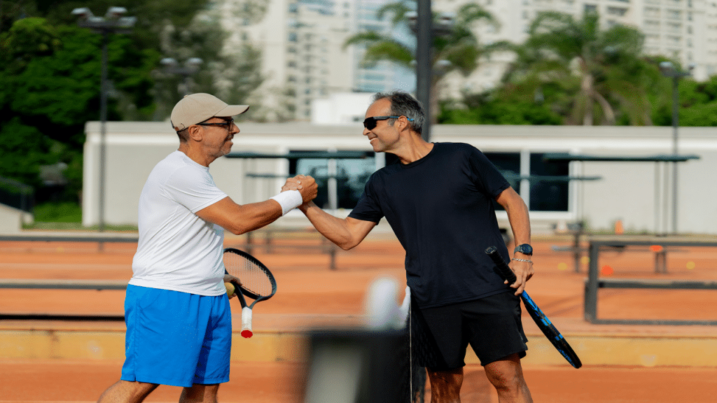 A pair of middle-aged men in sportswear shake hands on a tennis court after a match.