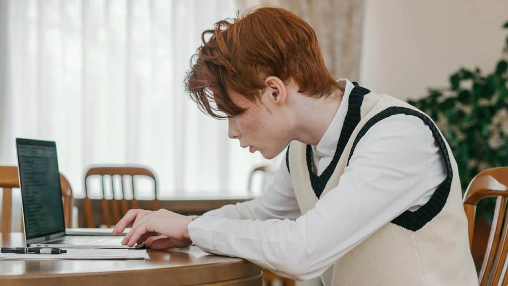A man slouching while using his laptop as he sits at a table.