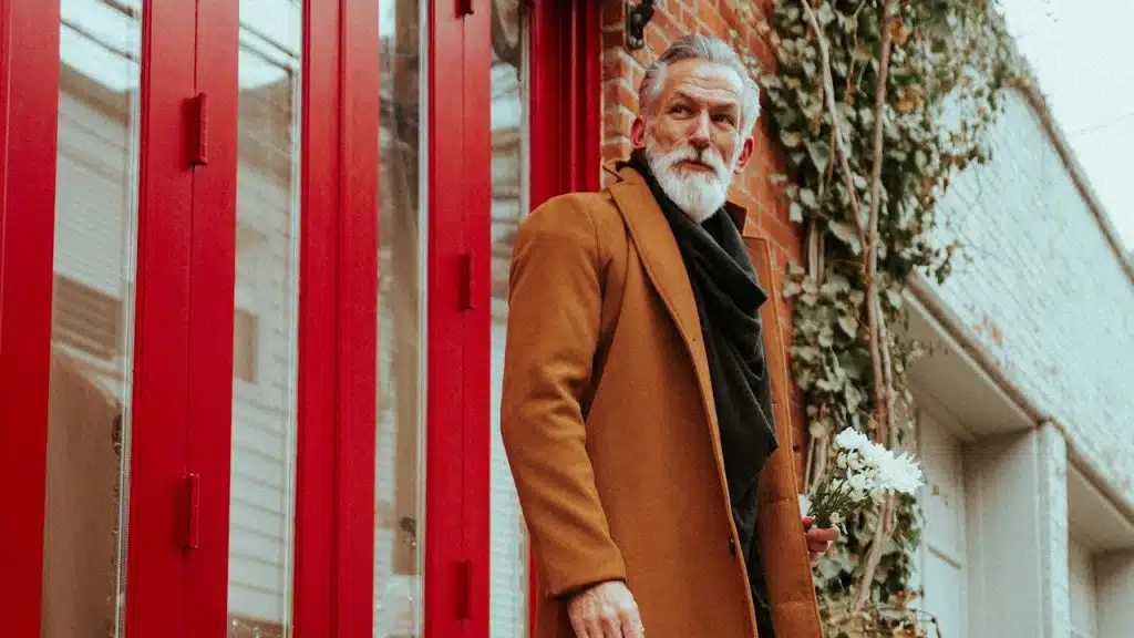 A stylish older man with a beard standing outdoors and looking to the side.