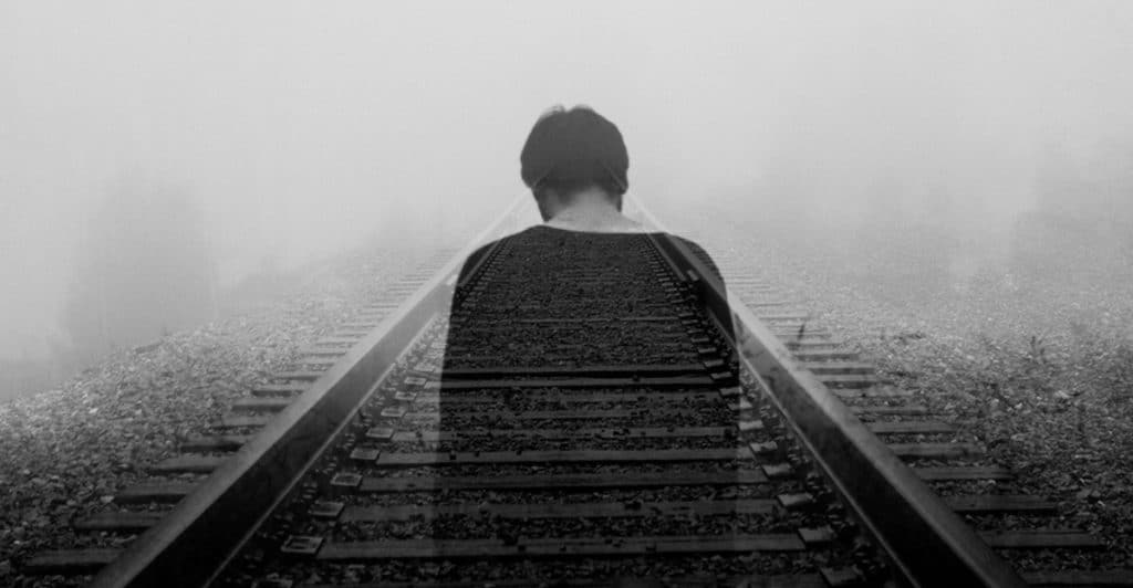 A man looking sad by the train tracks.
