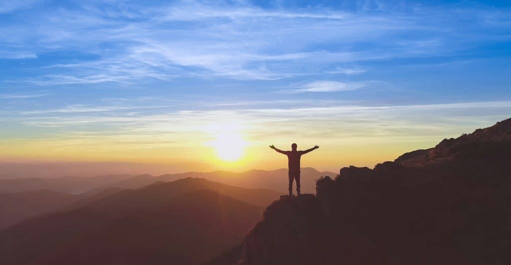 A man with his hands up while watching the sunset.