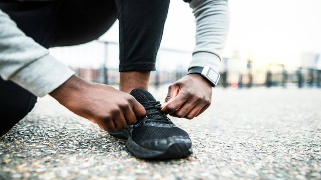 A close-up of a person tying a black running shoe while wearing a smartwatch.