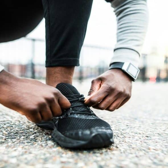 A close-up of a person tying a black running shoe while wearing a smartwatch.
