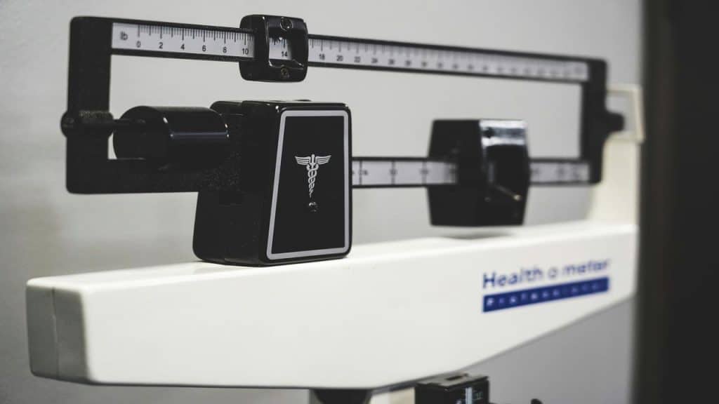 A close-up of a mechanical beam scale used for measuring body weight, featuring a caduceus symbol and labeled “Health o meter.”
