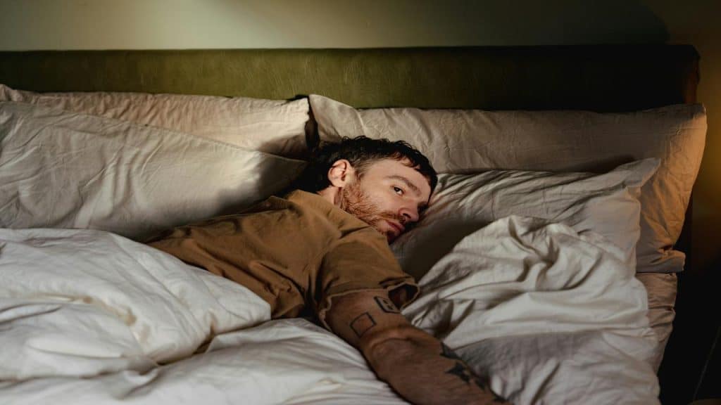 A man lying in bed, awake and glancing at something.