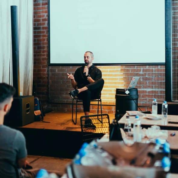 A man holding a mic speaking to a room full of people