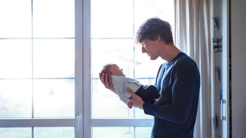 Man smiling while holding a baby onesie