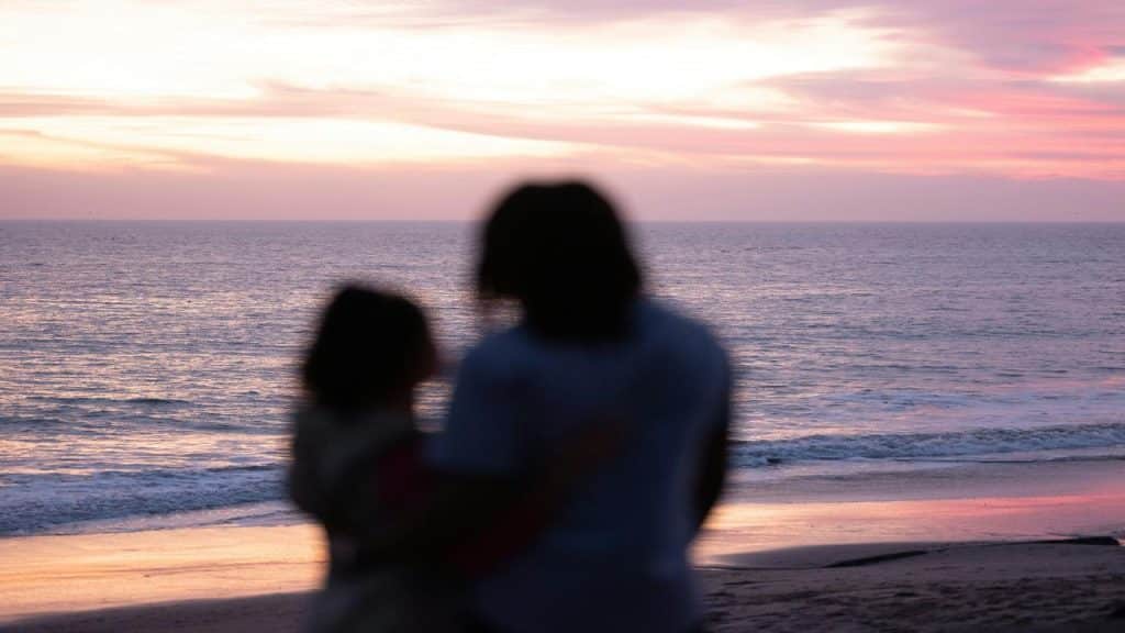 A silhouetted couple stands on the beach, watching a colorful sunset over the ocean.