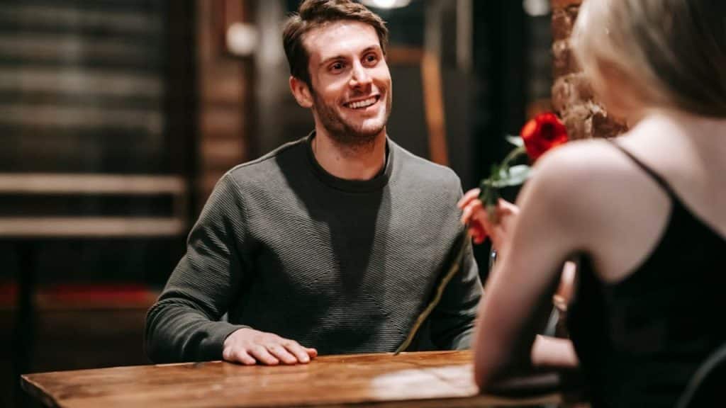 Couple recreating their first date where a man handing a rose to a woman in a familiar café.