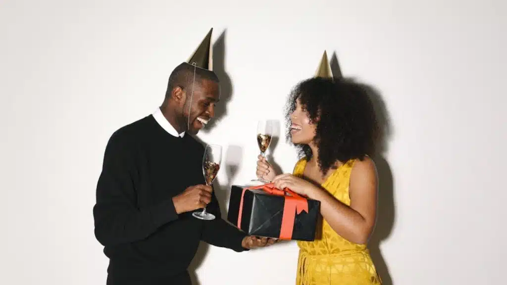 A man giving a gift box to a woman with a handwritten note on top while smiling.