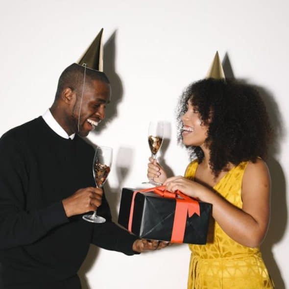 A man giving a gift box to a woman with a handwritten note on top while smiling.