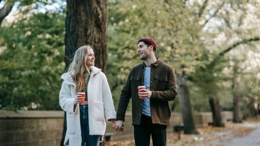 Couple walking hand in hand on a planned date with coffee and smiles.