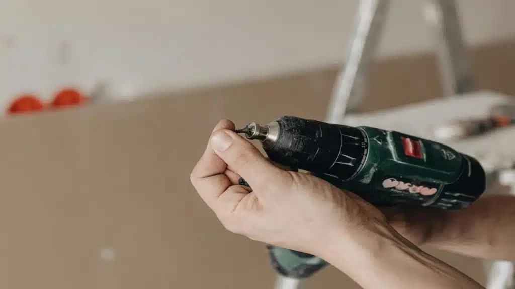 A person holding a power drill with one hand and a screw on the other.