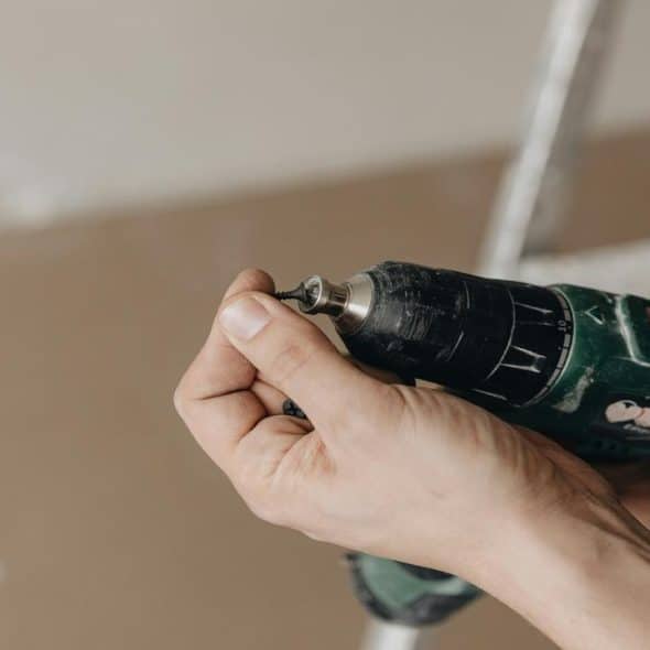A person holding a power drill with one hand and a screw on the other.