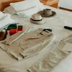 An outfit with a beige suit, brown shoes, hats, and accessories laid out on a bed.