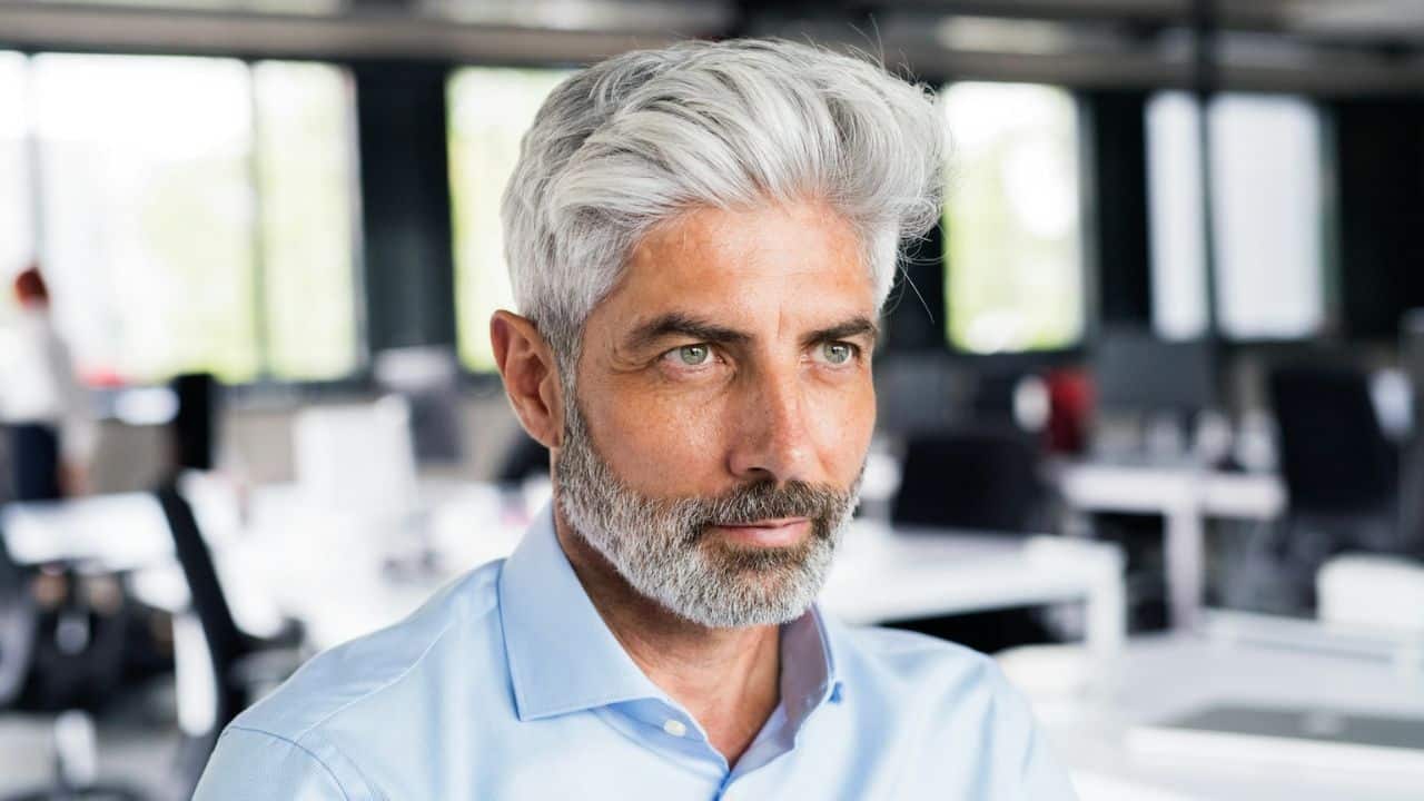 A middle-aged man with grey hair and beard looks to the right.