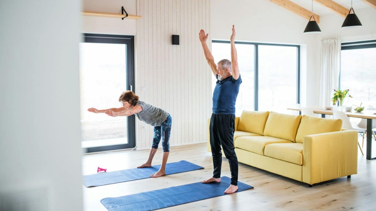 A man and a woman are doing yoga on blue mats in a modern living room.
