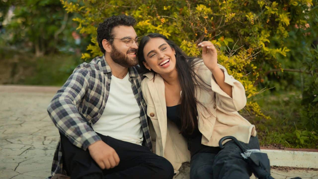 A happy couple is sitting outdoors, smiling and laughing together.