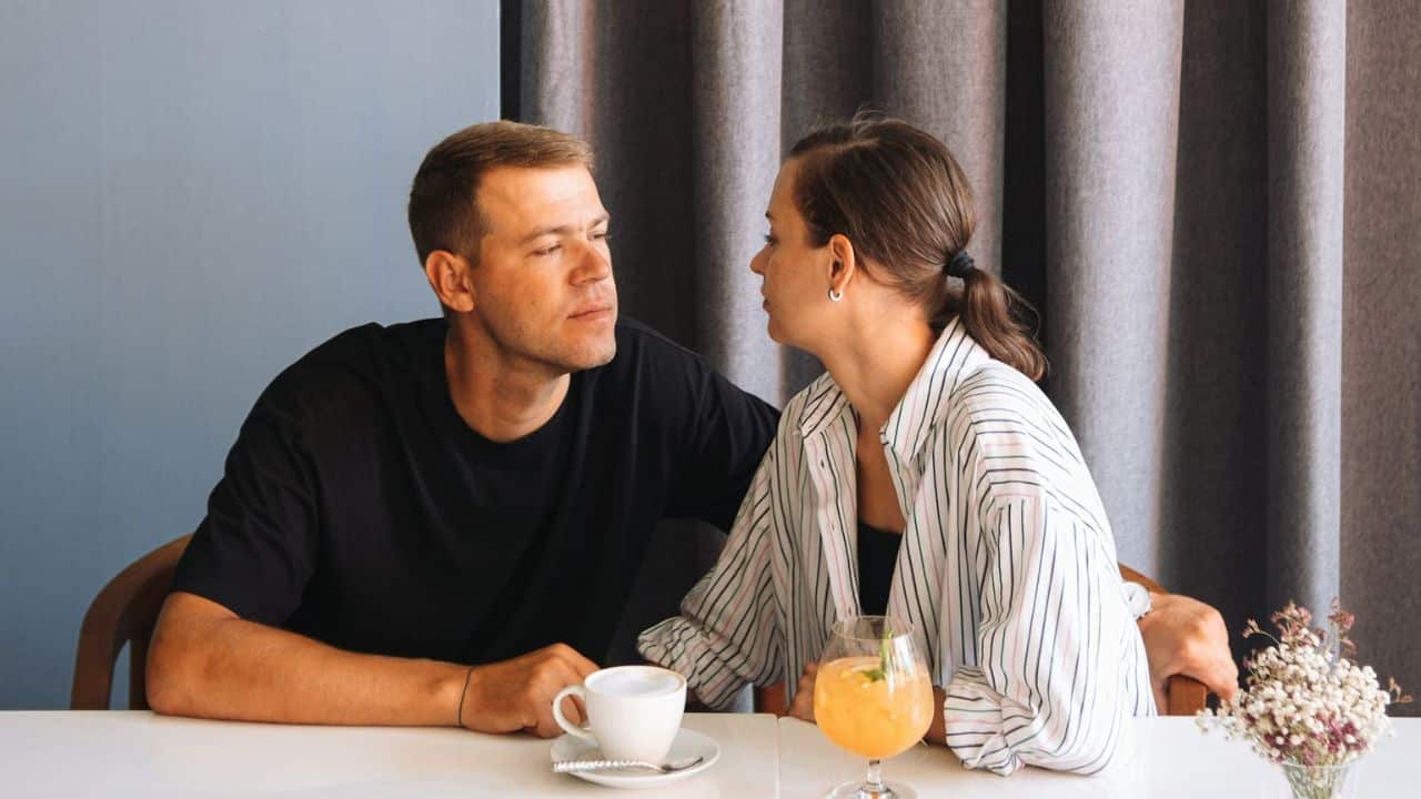 A man and woman sit at a table, looking at each other, with drinks in front of them.