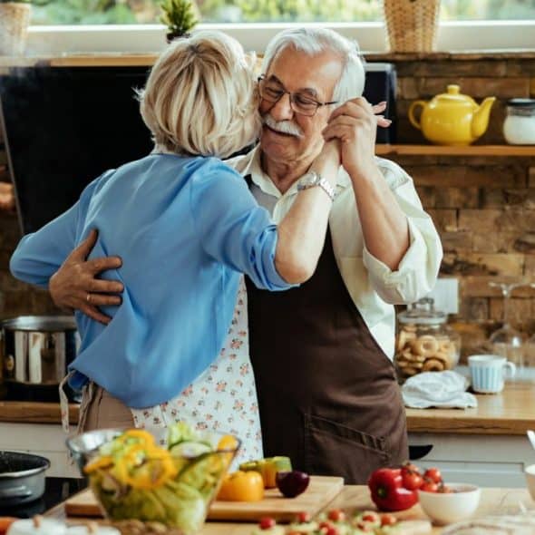 A joyful older couple slow dances in a rustic kitchen filled with fresh ingredients.