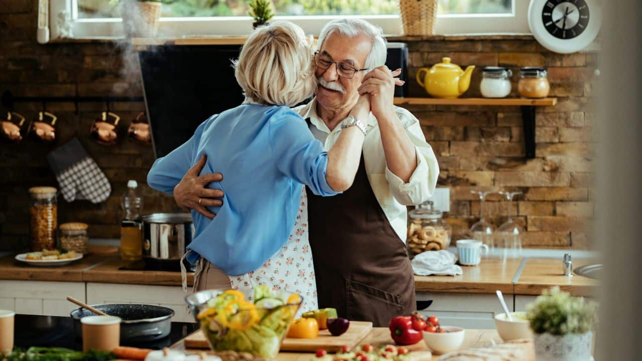 A joyful older couple slow dances in a rustic kitchen filled with fresh ingredients.