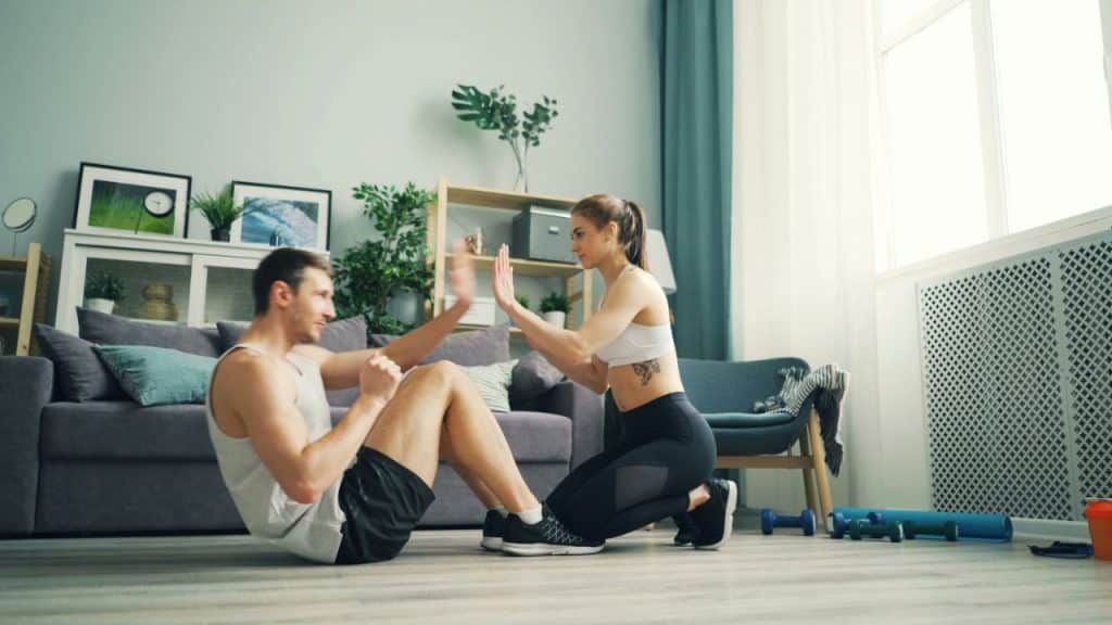 A man does sit-ups while a woman in athletic wear gives him a high-five.