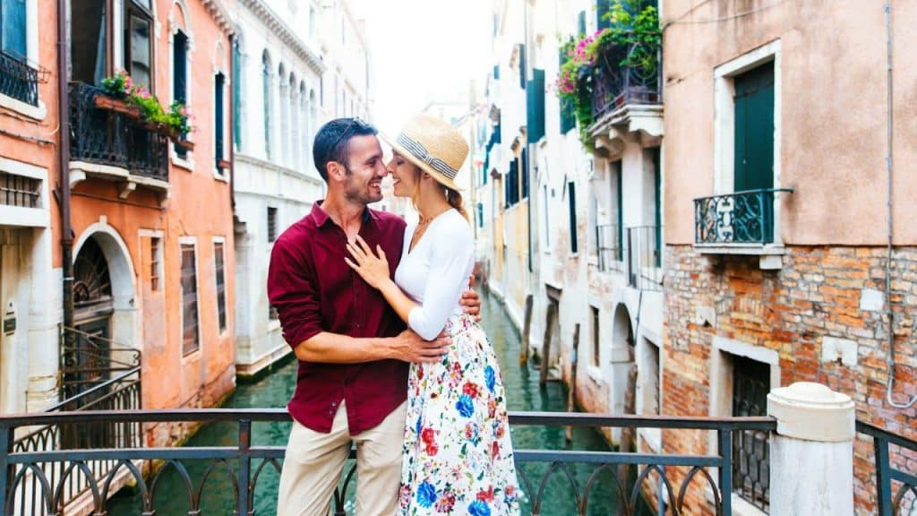 A happy couple embraces on a bridge over a canal, surrounded by old buildings.