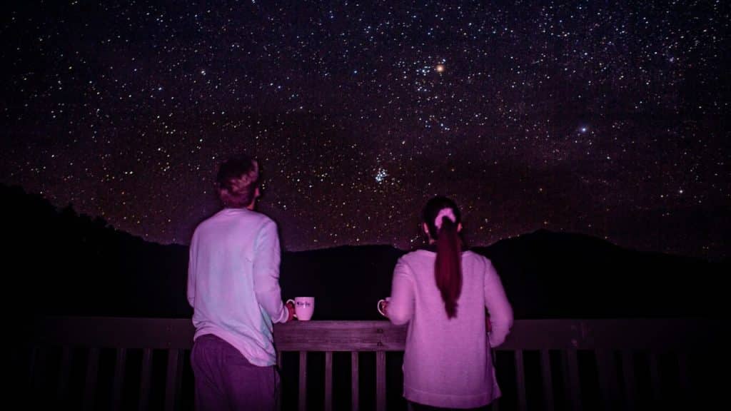 A couple stands on a balcony, gazing up at a sky full of stars.