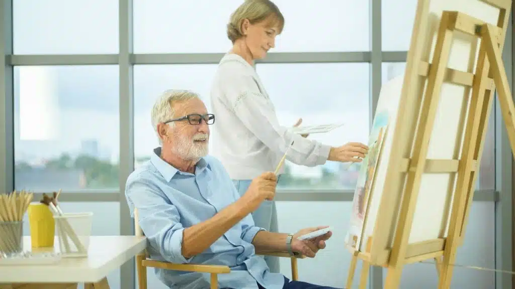 A man sits and paints on a canvas while a woman stands behind him, also painting.