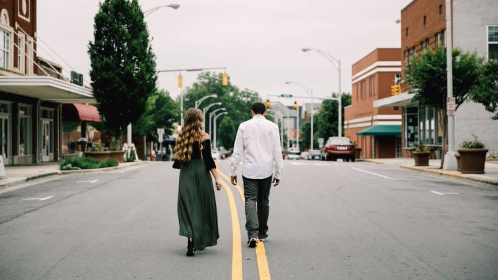 A woman in a long skirt and a man in a white shirt walk down a street.