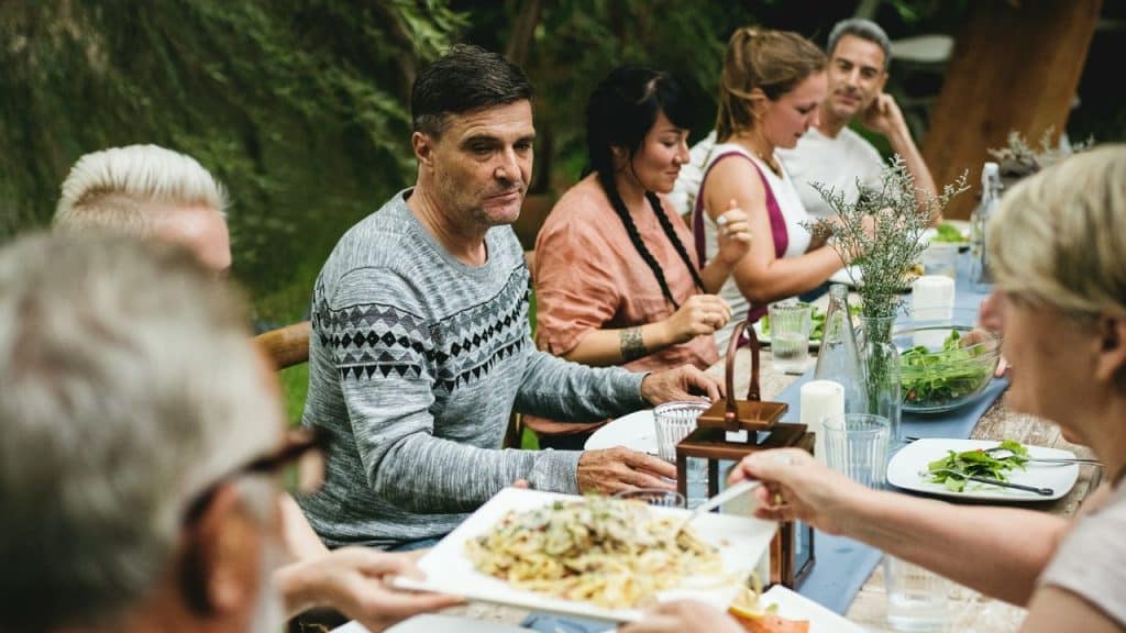 A group of people are seated at a long outdoor table, enjoying a meal together.