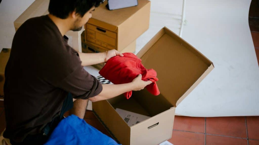A man puts a red piece of clothing into a cardboard box.