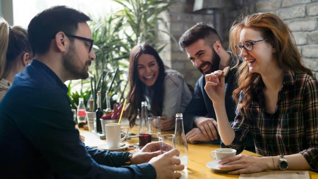 A group of four young adults are laughing and talking around a table at a cafe.