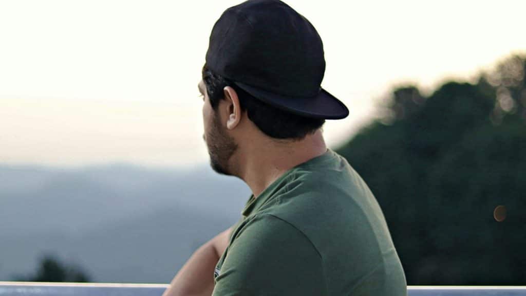 A man wearing a backwards black baseball cap and a green t-shirt looks out into the distance.