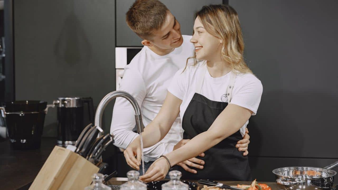 ALT Text: Couple smiling after resolving a disagreement calmly near the kitchen sink.