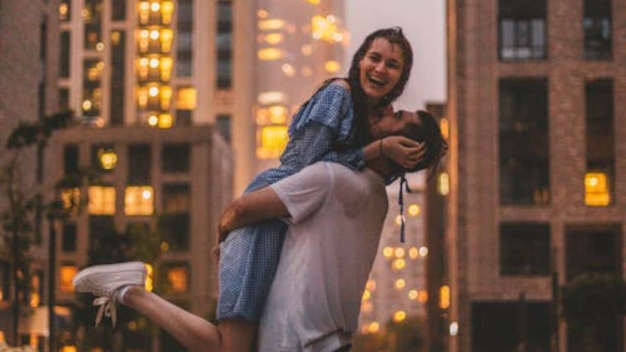 Couple smiling and holding each other close with city lights glowing behind them.