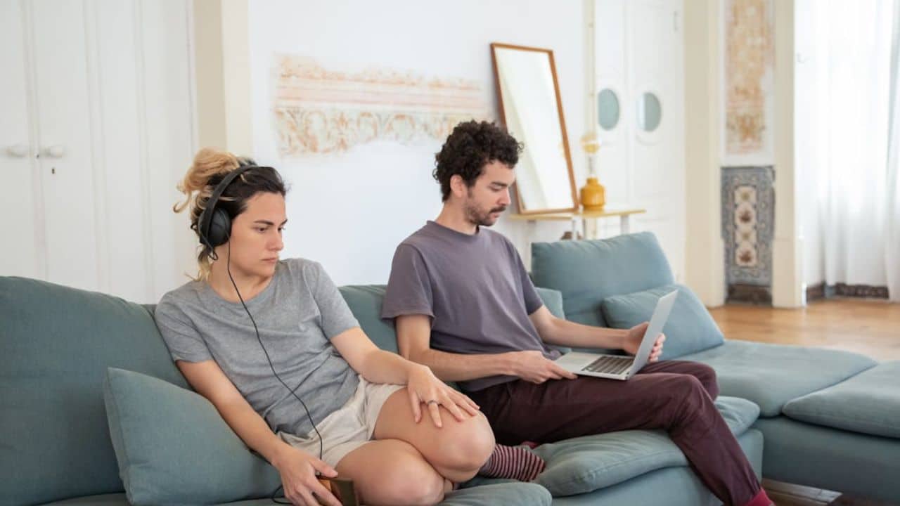 Man working on his laptop while the woman is listening to music.