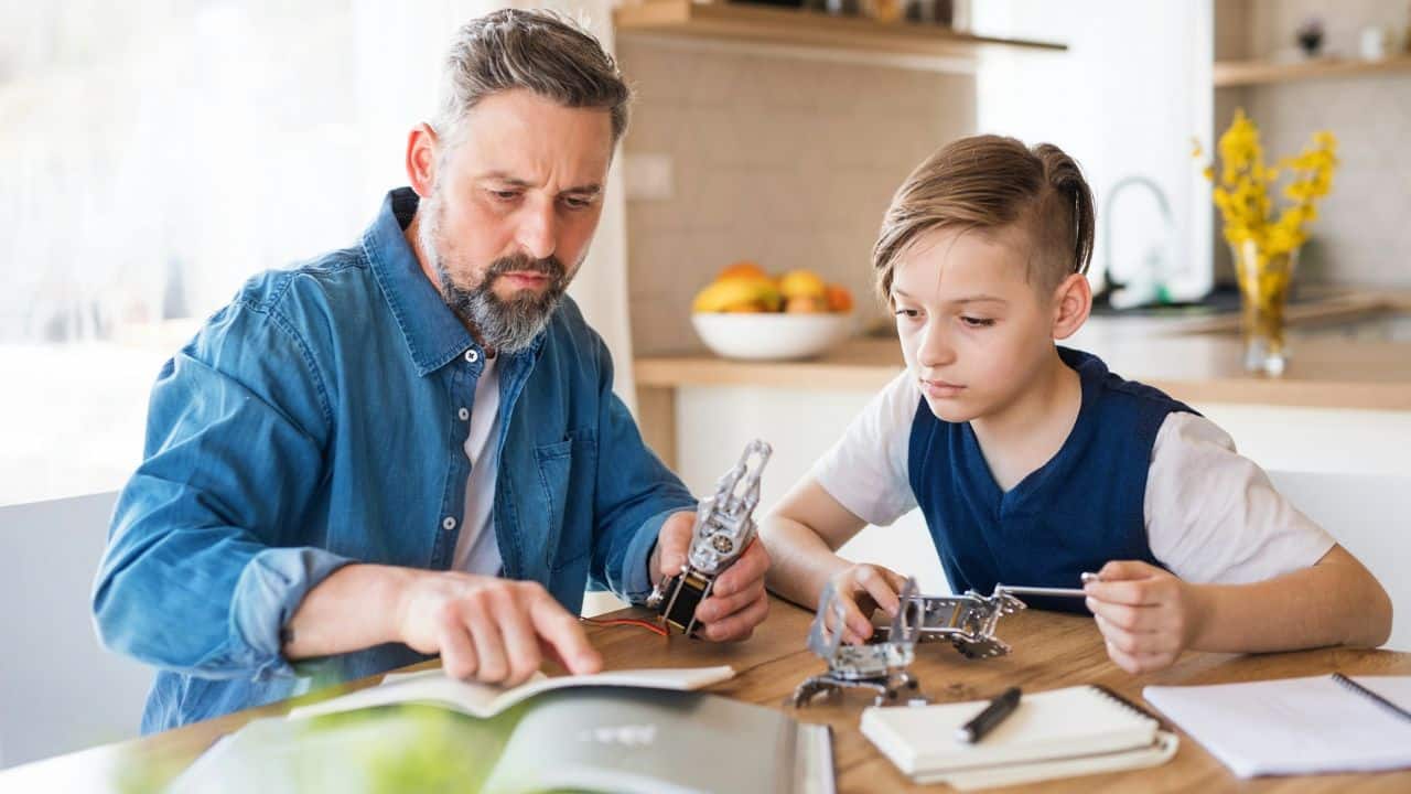 A bearded man and a boy sit at a table, looking at instructions and holding robot parts.