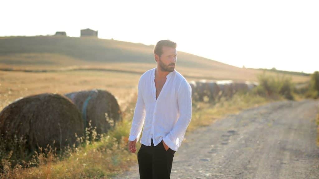 A man standing alone on a quiet street at sunset, deep in thought.