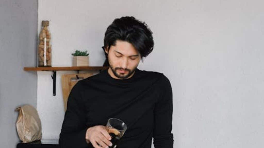 A man in black holding a drinking glass reflecting on his role in a breakup.