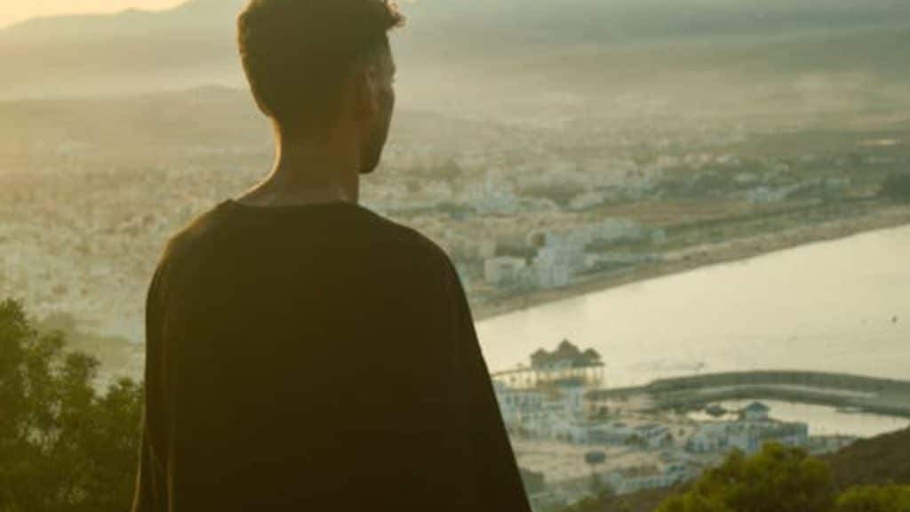 Man standing at a scenic overlook at sunrise with a calm, determined expression.