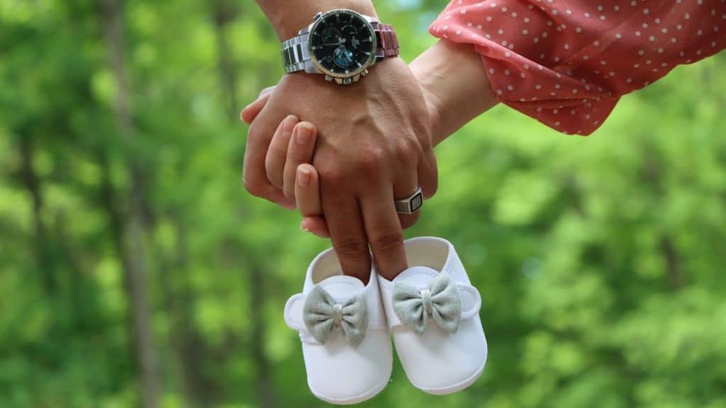 Couple walking in the park planning future goals and holding shoes of a baby.