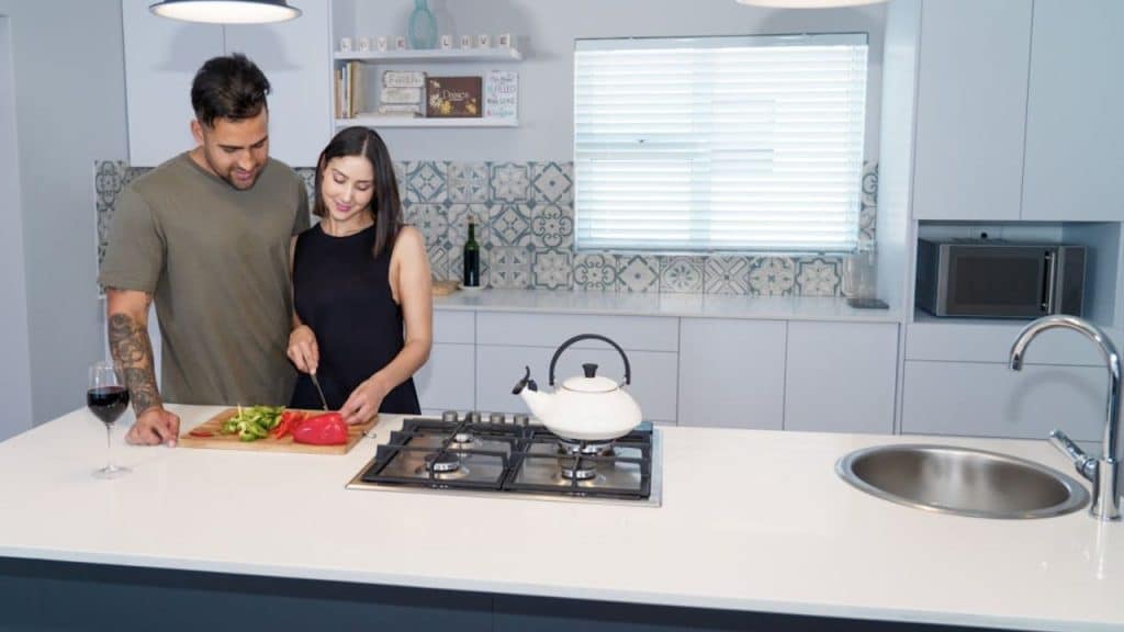 Man in his 40s smiling with a woman while cutting vegetables.