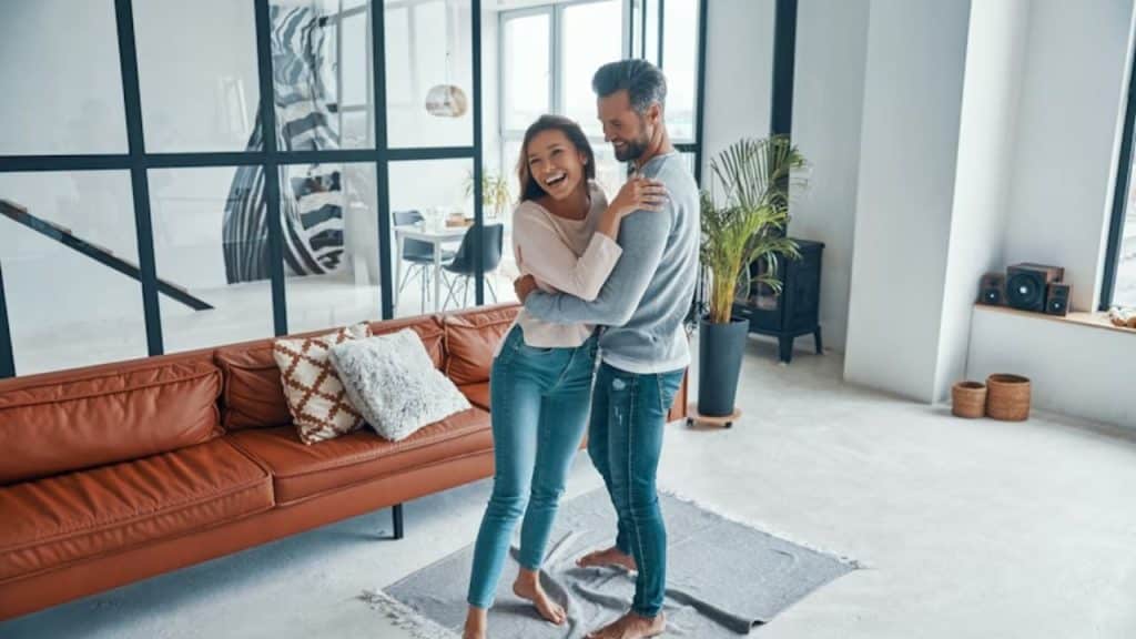 Couple in their 40s laughing while dancing in the living room.