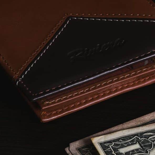 A brown leather wallet, a black Riviera watch, and dollar bills on a dark surface.