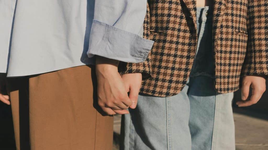 A close-up of two people holding hands, wearing casual and patterned clothes.