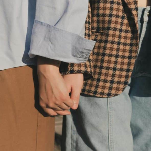 A close-up of two people holding hands, wearing casual and patterned clothes.