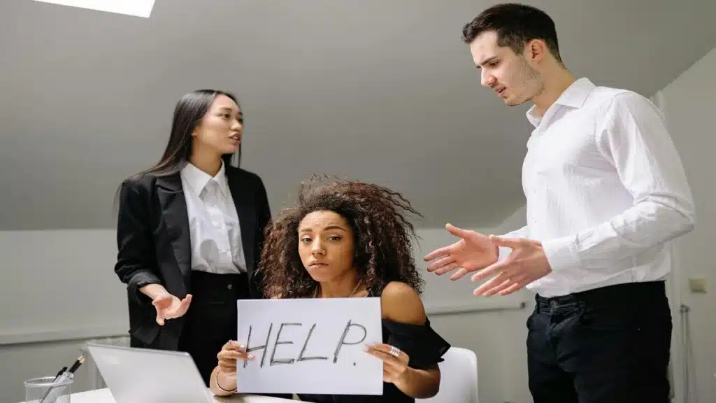 A woman holding a sign saying “help” while her colleagues fight.
