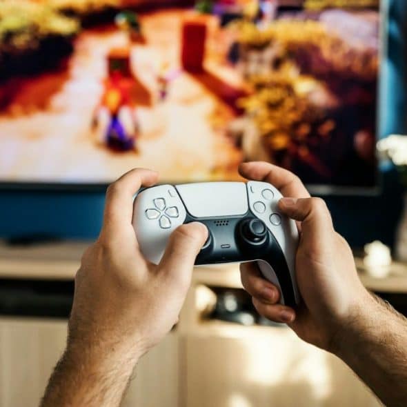A person holds a white video game controller, playing a game on a TV.